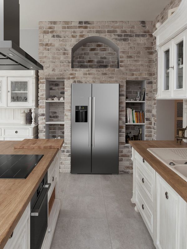 Galley kitchen with oak countertops and classic white cabinetry. An exposed brick wall with a stainless steel French door fridge is located in the background.