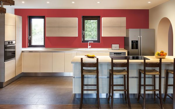 Cocina en forma de L con isla, gabinetes color crema, electrodomésticos de acero inoxidable y una pared roja