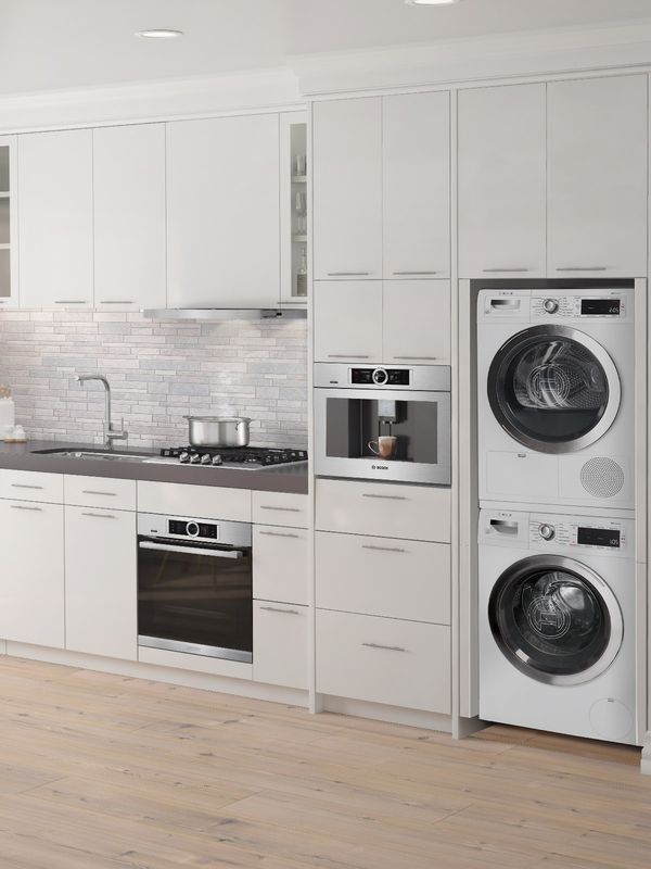 Small one-wall kitchen with plentiful storage and built-in appliances, including a stacked washer and dryer combo. A white brick backsplash and stainless steel accents create a clean overall look.