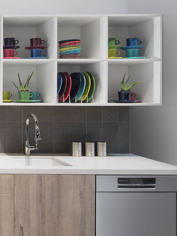 Bucătărie mică cu dulapuri din lemn, panou de protecție la stropire din ceramică gri texturată și rafturi deschise cu tacâmuri colorate. Mașină de spălat vase, cuptor independent și hotă din inox