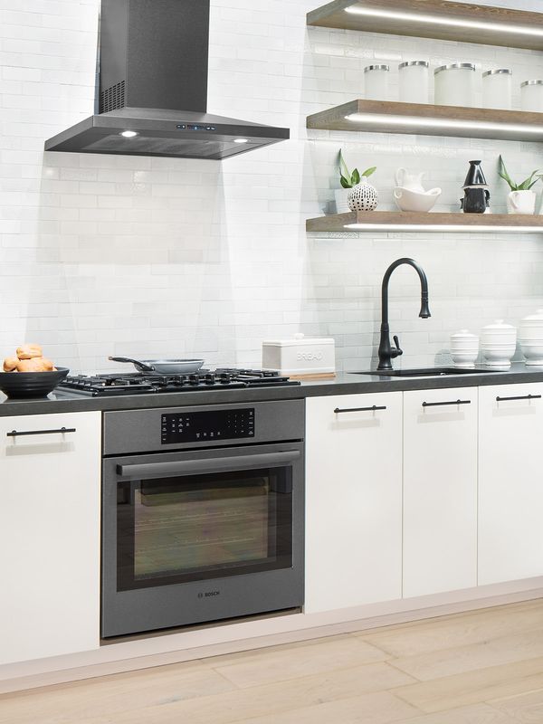 Bucătărie alb-negru cu electrocasnice din oțel inoxidabil negre, inclusiv o mașină de gătit cu hotă și mașină de spălat vase. Două rafturi deschise luminează zona de lucru