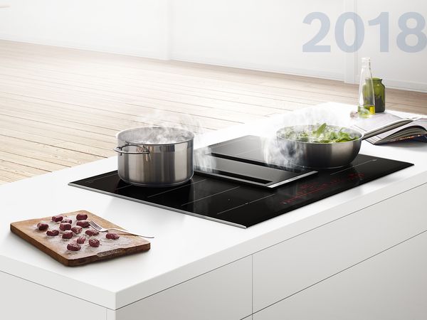 Hvit kjøkkenøy med integrert ventilasjonsplatetopp som absorberer damp fra sautering av grønnsaker.