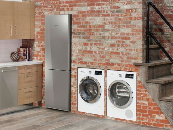 Bosch kompaktiškas skalbyklės-džiovyklės duetas, įmontuotas įstrižai plytinėje sienoje kartu su įmontuojamuoju nerūdijančio plieno šaldytuvu