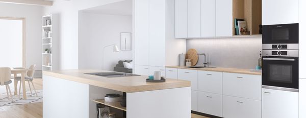 Contemporary white island kitchen with flowing lines, built-in appliances and an oven installed at eye level with an open seating area in the background