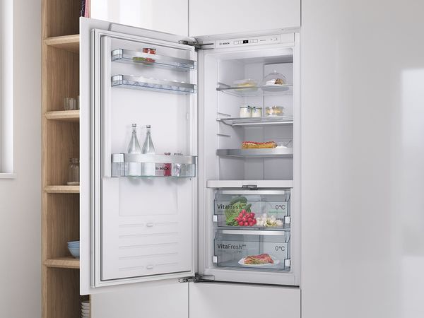 Pequeño frigorífico integrado en armarios blancos con un estante de madera abierto detrás