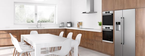 All-white U-shaped kitchen with a wood countertop and modern appliances. Side-by-side fridge-freezer with open doors filled with frozen items and colourful produce