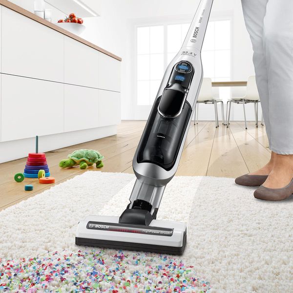 A cordless vacuum vacuums up confetti. There are toys in the background.