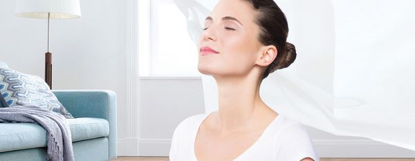 Person with their eyes closed, breathing in. Bright background with sofa and lamp