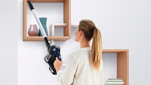 A woman vacuums a shelf with a handheld vacuum cleaner.
