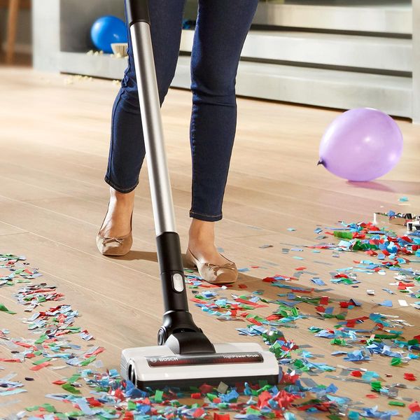 A woman vacuums confetti with a cordless vacuum cleaner. There are balloons everywhere.