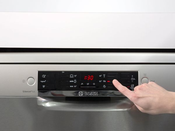 Una persona inicia un programa en el lavavajillas, utilizando los botones de la pantalla de un lavavajillas Bosch