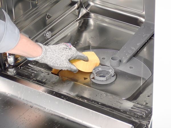 En hand använder en svamp för att suga upp vatten från botten på en Bosch diskmaskin