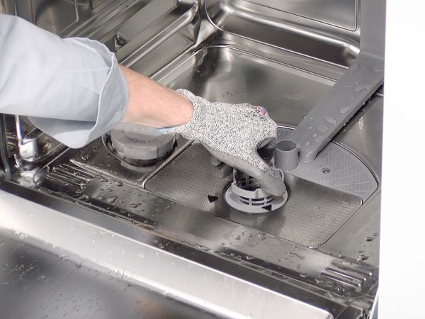 Person wearing protective gloves unlocking the filter unit at the base of a dishwasher 