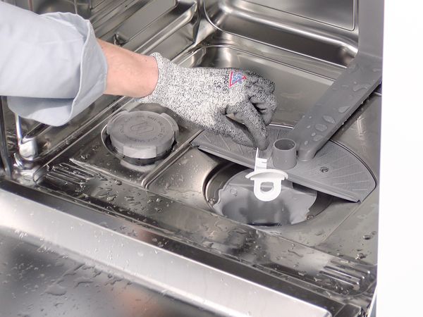 A hand with protective glove removing the pump cover from a Bosch dishwasher