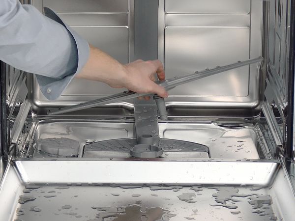 En person demonterer en spylearm fra en Bosch oppvaskmaskin