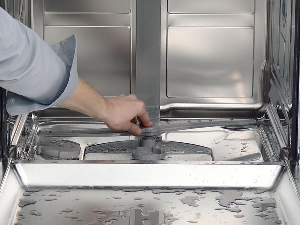 Egy személy, aki a mosogatógép permetezőkarját a helyére pattintja.