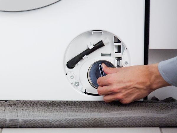 Persoon die het pompdeksel van een Bosch-wasmachine losschroeft
