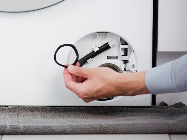 En person rengjør delene til en Bosch vaskemaskin