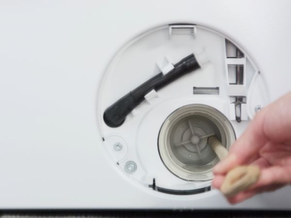 En person kontrollerar att hjulet till en dräneringspump snurrar fritt i en tvättmaskin. 