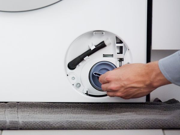 Eine Person setzt den Pumpendeckel einer Bosch Waschmaschine wieder ein.