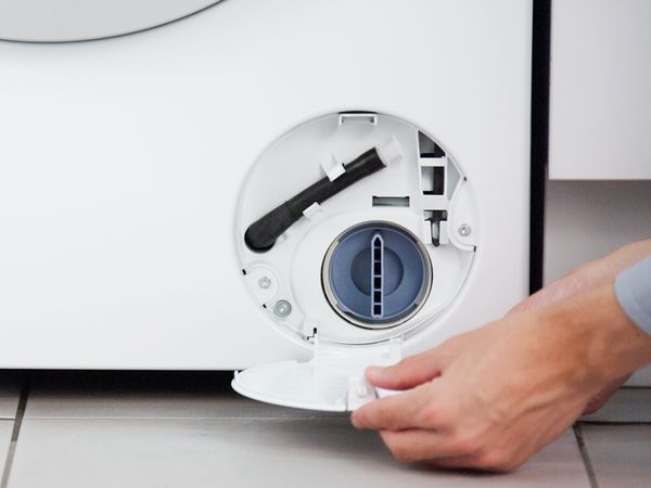 En person stänger serviceluckan till en tvättmaskin