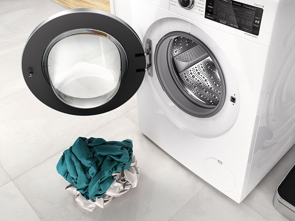 Bosch vaskemaskin med åpen dør og en liten haug med klesvask foran
