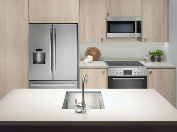 Stainless-steel fridge and cooking appliances arranged in a perfect triangle with a sink placed on an island at centre front  