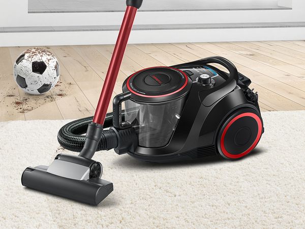 Bosch bagless ProPower vacuum on beige carpet, dirty football in the background on hardwood floor