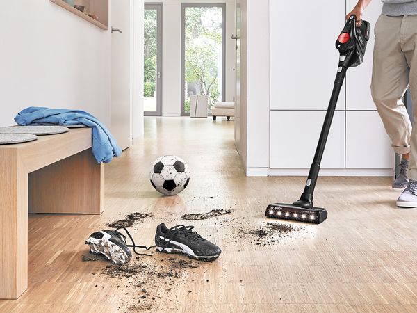 Mężczyzna używający bezprzewodowego odkurzacza Unlimited ProPower marki Bosch do sprzątania zabrudzeń z korków piłkarskich i piłki