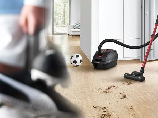  Bosch Staubsauger mit Beutel der Produktreihe ProPower und ein Fußball neben schmutziger Unordnung auf einem Hartholzboden