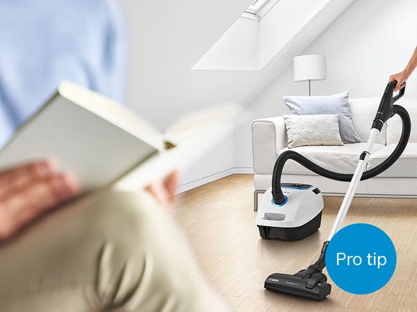 Person cleaning living room with bagged Bosch ProSilence vacuum while someone else reads