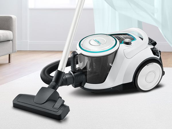 Close-up of a white ProHygienic vacuum on a beige living room rug in front of an open window