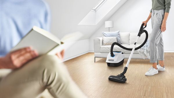 Eine Frau reinigt den Parkettboden im Wohnzimmer mit einem Bosch Staubsauger. 