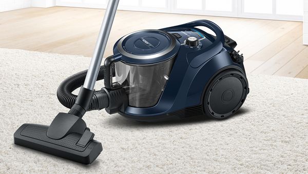 Dark blue bagless vacuum on a living room rug.