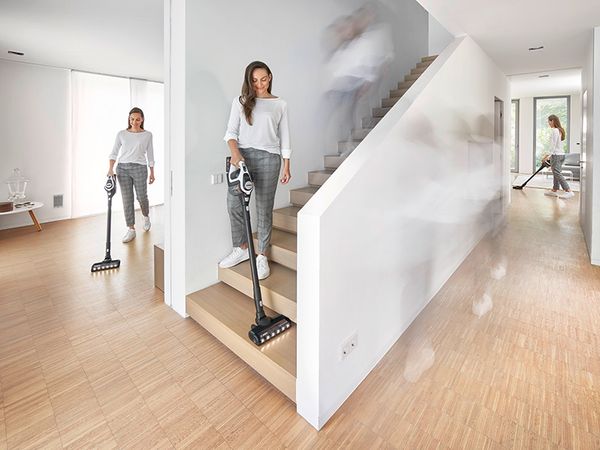 The same woman is vacuuming a house in three different spots with an hanheld vacuum.