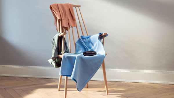 Auf einem Stuhl gestapelte Kleidungsstücke, auf denen der FreshUp-Textilerfrischer liegt. 