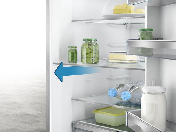 Nahaufnahme der Ablagen im Innenraum eines Kühlschranks. Der Pfeil gibt an, wie die Böden für die Reinigung herausgenommen werden können.
