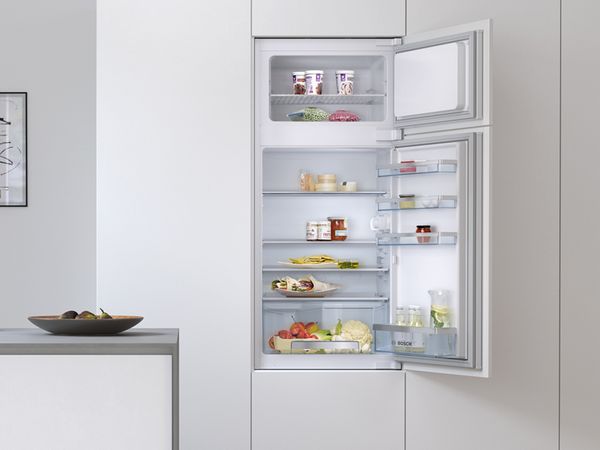 Kalustepeitteisen Bosch-jääkaappipakastimen avoimesta ovesta näkyy elintarvikkeita ja juomia.