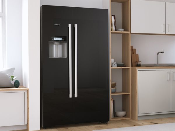 Черный отдельностоящий холодильник типа side-by-side на яркой современной кухне.