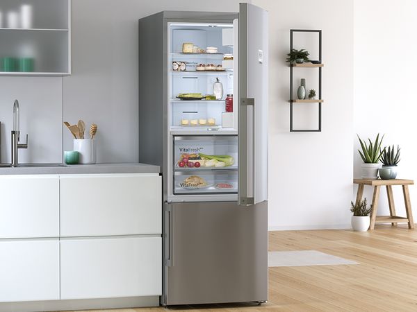 Brīvstāvošs Bosch ledusskapis ar saldētavu sudraba krāsā baltā virtuvē.