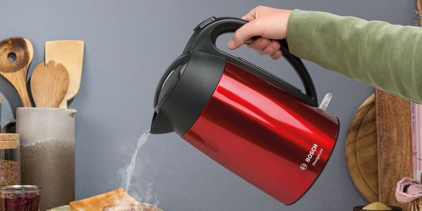 DesignLine waterkoker, in rood en inox. Person pours hot water into a pot.
