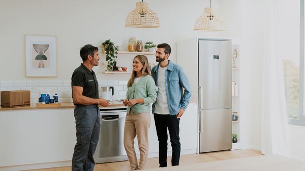 Farbenfrohe Bosch Hausgeräte Symbole schweben in einer offenen Küche neben einem Kühlschrank.