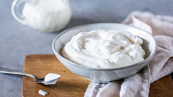 A bowl of fluffy whipped cream next to a spoonful of whipped cream.