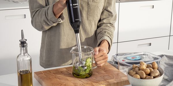 Person standing at worktop using a Bosch hand blender to puree in a beaker.