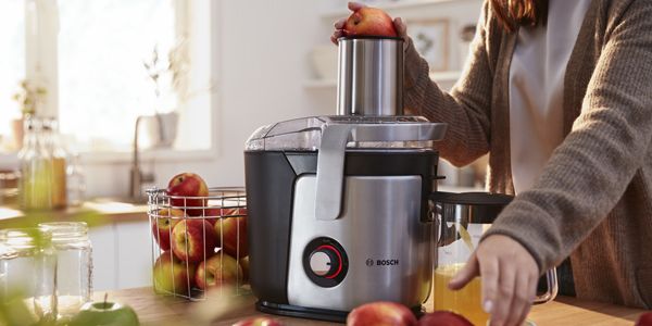 En person står ved en kjøkkenbenk og presser epler i en Bosch juicepresse.