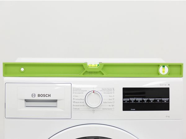 Un niveau à bulle vert posé sur le rebord avant d’un lave-linge Bosch.