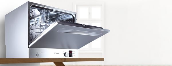 Lave-vaisselle de comptoir Bosch en acier inoxydable avec la porte légèrement ouverte sur un plan de travail.