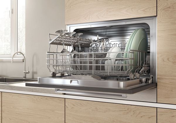 Lave-vaisselle compact encastrable Bosch dans un meuble avec vue intérieure d'un panier plein.