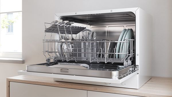 Un lave-vaisselle de comptoir avec une porte ouverte et un panier complet sur un plan de travail de cuisine.