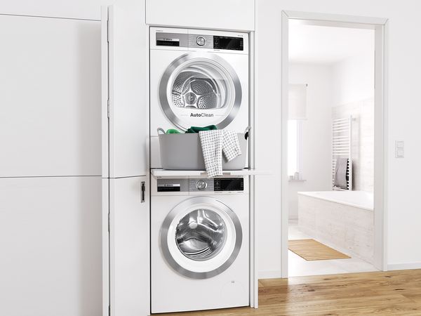 Päällekkäin oleva pyykinpesukone ja kuivausrumpu integroituna valkoiseen kaappiin, jonka päällä on pyykkikori.